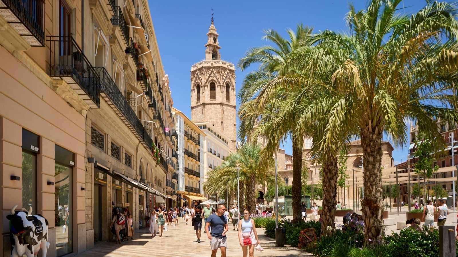 Personas caminando en la Plaza de la Reina, con tiendas y terrazas de fondo